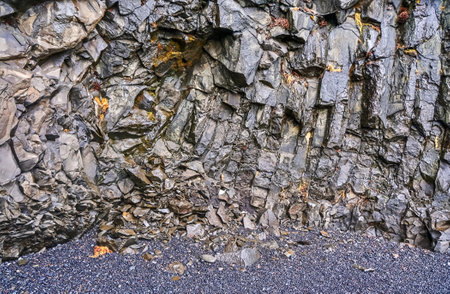 Basalt rock face towering over a black sand beach in iceland, showcasing geological formations