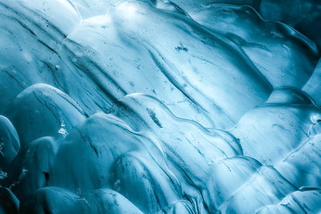Light filtering through the ice creates a mesmerizing blue glow inside a stunning ice cave in...