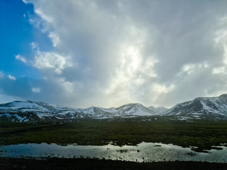 Snow capped mountains rising above a green valley under a cloudy sky in the beautiful icelandic landscapeの写真素材
