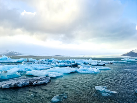 Ice floes drifting gracefully in jokulsarlon glacier lagoon, surrounded by a cloudy sky and the...