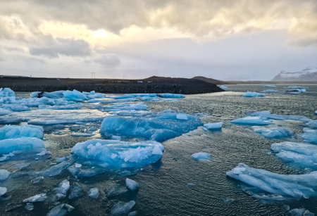 Blue icebergs are floating on the jokulsarlon glacier lagoon in iceland under a cloudy sky during...