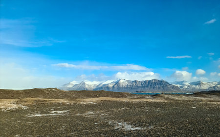 Snow capped mountains rise majestically above a vast, desolate desert landscape in iceland, under a...