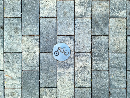Metallic bicycle symbol embedded in a grey cobblestone pavement, indicating a designated cycling area or pathの写真素材