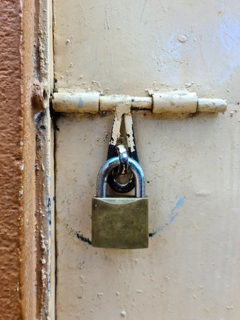 Close-up of a padlock fastening a metallic latch on a weathered beige door, suggesting security...