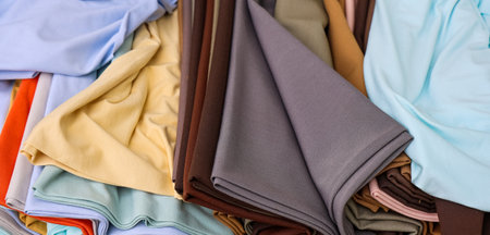 Cloth fabrics stacked presenting various textures and colors, offering a wide selection for fashion...