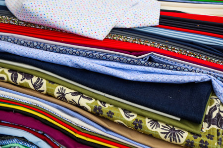 Many different fabrics are stacked, showcasing a variety of colors, patterns, and textures, ideal...