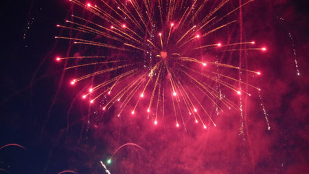 Bursting with red and gold colors, vibrant fireworks illuminate the night sky, creating a joyful and...