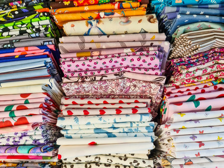Multiple stacks of colorful patterned fabrics showcasing a variety of designs, textures, and colors,...