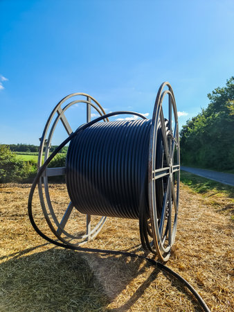 Black cable drum sitting on a field, ready for fiber optic cable installation, representing connectivity and technological advancement in rural areasの写真素材
