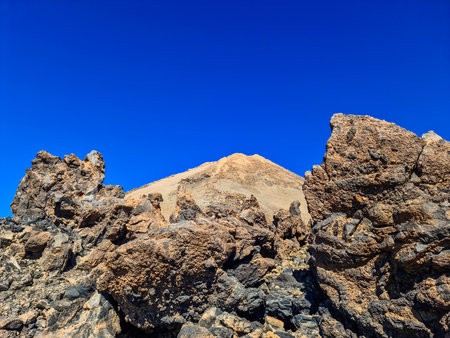 Barren volcanic landscape showcasing Mount Teide peak with rugged rock formations under a clear, intense blue skyの写真素材