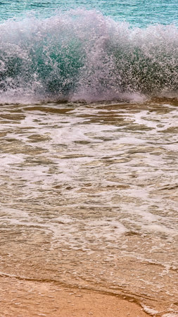 Ocean wave crashing with force on a tropical sandy beach, creating a beautiful display of splashing...