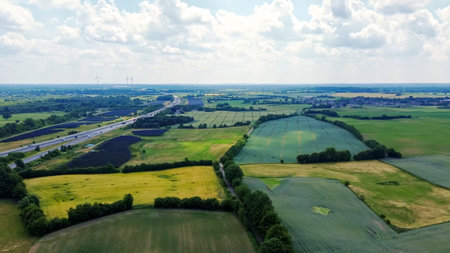 Rural landscape showing green fields, solar panels, moving traffic on a highway, and wind turbines