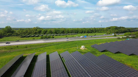 Solar panels line a green field next to a multi lane highway with moving vehicles under a blue sky