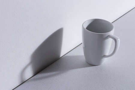 Empty White ceramic mug on white table with shadow on lonely wall without texture view from aboveの写真素材