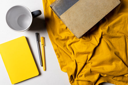 yellow fabric with book and gray cup next to gray and yellow pencil with hard shadows representing...