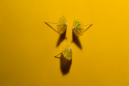 Yellow summer cocktail paper umbrellas on yellow table and in strong sunlight with casting shadow