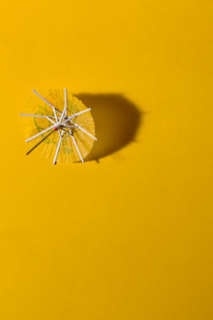 Yellow summer cocktail paper umbrellas on yellow table and in strong sunlight with casting shadowの写真素材