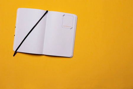 Notebook open in the middle with black separator and with a drawing of a frame on one of the sheets on a yellow backgroundの写真素材
