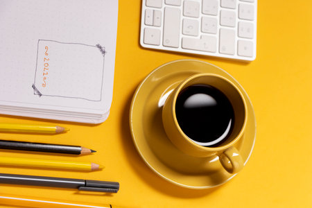 Notebook keyboard and cup with coffee on yellow background along with tools for making bullet journalの写真素材