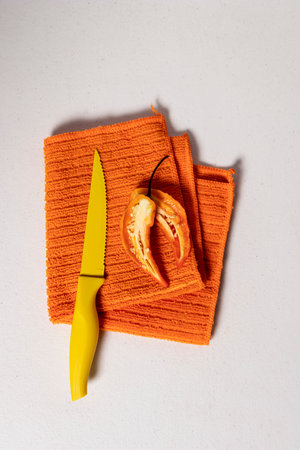 Orange bell pepper cut in half nest to a yellow knife on orange textured kitchen towel foldedの写真素材