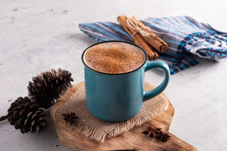 blue cup on vintage white wooden table accompanied by pine cones and blue cloth with cinnamon on topの写真素材