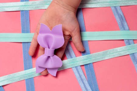 Little girl's hand holding a purple bow on a pink background
