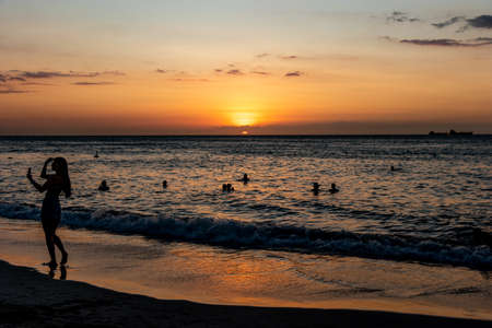 Women at sunset on the beach taking with cellphone taking a self portraitの写真素材