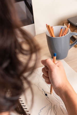 Man's hand drawing with a blue pencil on a notebook