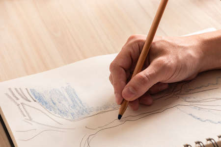 Man's hand drawing with a colored pencil on a notebook