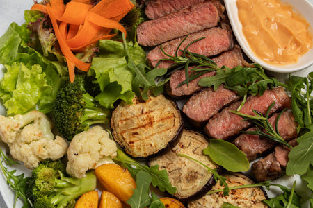 This professional food photograph features a delicious ribeye steak and a generous portion of roasted potatoes, artistically arranged on a white plate. The steam rising from the hot food adds a sense of warmth and freshness, making it a compelling image for advertising or print media.の写真素材