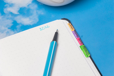 Flat lay composition featuring a blue-ink pen and a notebook with 2026 goals, all set under an...
