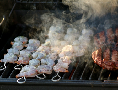 Skewered shrimp cooking  and smoking  on a barbecue grill along side beefの写真素材