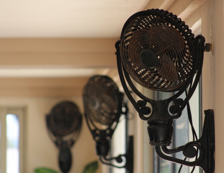 Three vintage fans mounted near the ceiling to provide a breeze in a very large room の写真素材