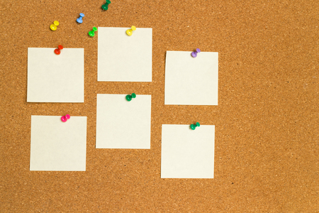 empty yellow post-it notes on cork board with color pinsの写真素材