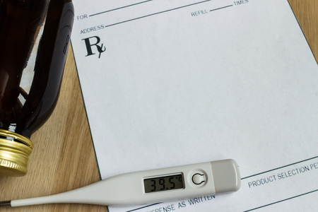 Digital thermometer with high temperature on blank prescription and bottle of syrupの写真素材