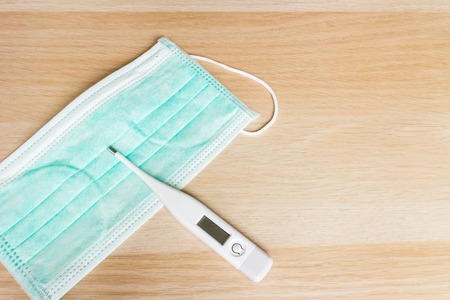 Disposable face mask with digital thermometer on wooden background
