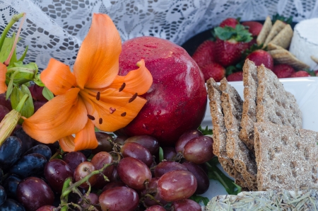 Presentation of grapes, pomegranite and strawberries with orange lilly and crackersの写真素材
