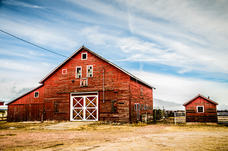 A classic red barn with white trim on Colorado plains set agianst a partly cloudy and blue sky のeditorial素材