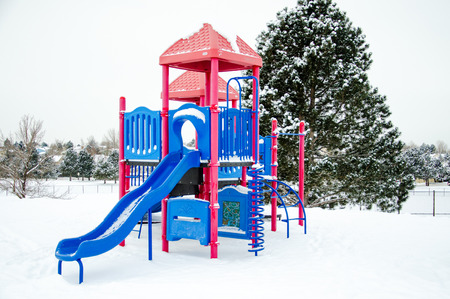 Horizontal view of red and blue neighborhood playground equipment after snow storm leaves fresh white snow on the playground の写真素材