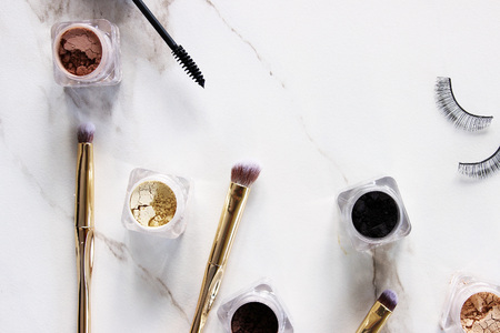 Loose eyeshadow in containers with gold brushes. White marble copy space.の写真素材