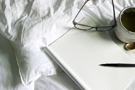 Above view of tea, notepad, pen and eyeglasses in a white bed.の写真素材