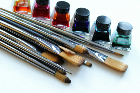 Large pile of silver metal paintbrushes with rainbow colored watercolor paints in background. Copy...