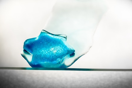 Blue piece of ice melting on a sheet of glassの写真素材