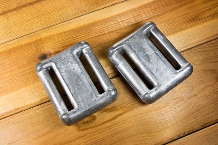 Two lead diving weights on wooden surface
