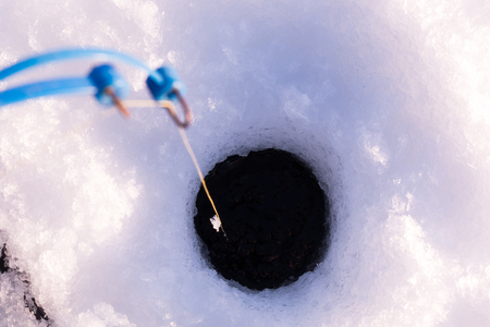 Ice fishing rod with line leading down to the hole on iceの写真素材