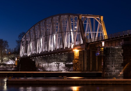 Nightly railroad bridge over streaming water with snowy surroundings.の写真素材