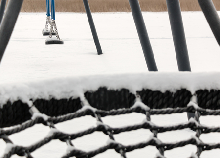 Snowy spiderweb-styled circular rope netting of a swing at a playgrond in winterの写真素材