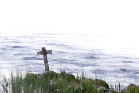 Wooden cross on a lake shore with white backgroundの写真素材