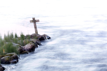 Wooden cross standing by a river with background fading to whiteの写真素材