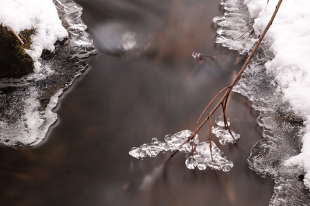 Ice formations on a branch in a small stream in winterの写真素材